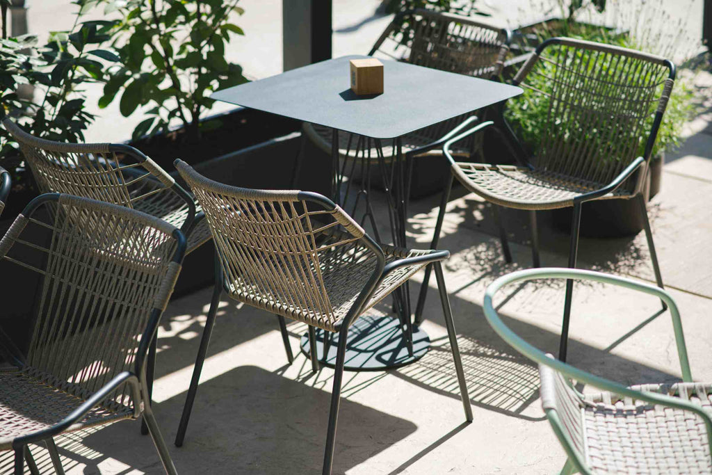 Outdoor-Szene mit mehreren stilvollen Gartenstühlen um einen quadratischen Tisch
